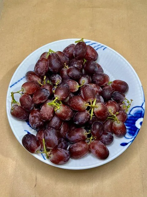 A white and blue bowl filled with red grapes