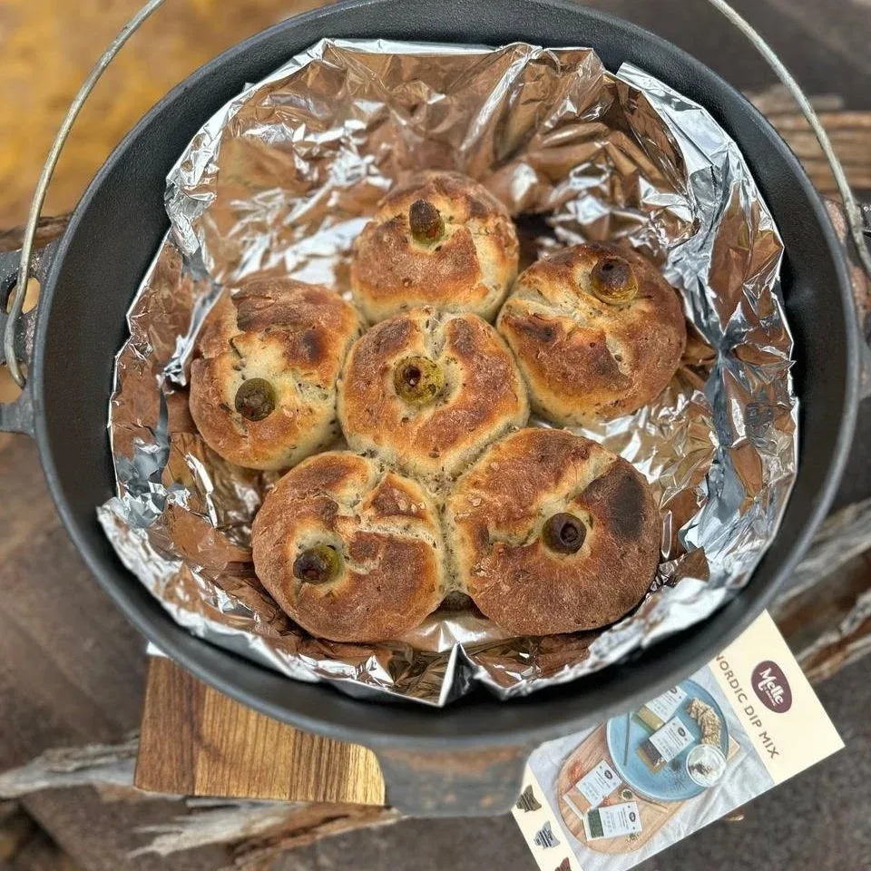 Six freshly baked bread rolls in a camp oven on top of a piece of wood with Mette is Baking Dip Mix