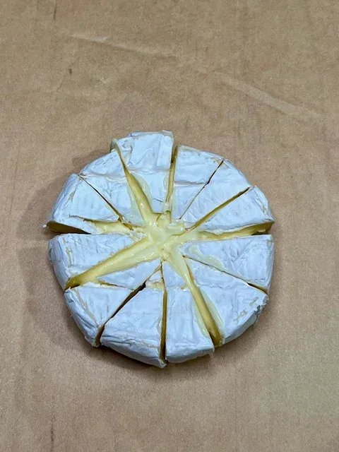 A wheel of camembert cheese cut into small wedges